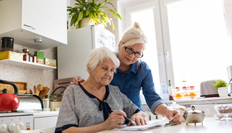 Woman Assisting her Elderly Loved One Fill out Paperwork Advance Care Planning for a Chronic Condition