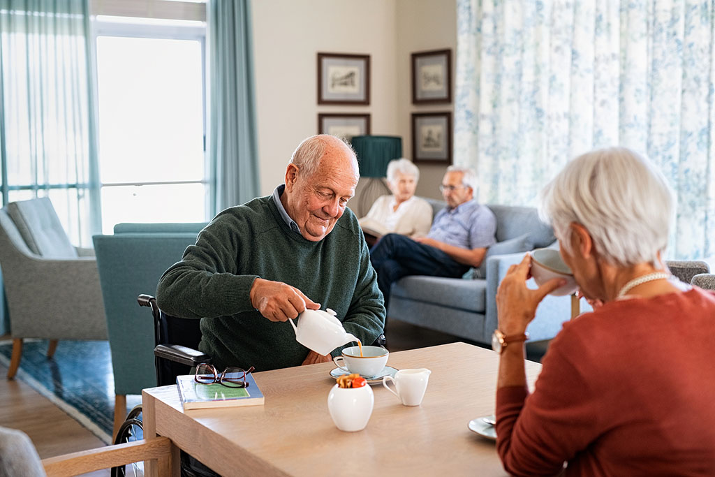 A Senior Man Sitting at a Table Pouring From a Teapot With a Senior Woman Across From Him What Does a Memory Care Community Do